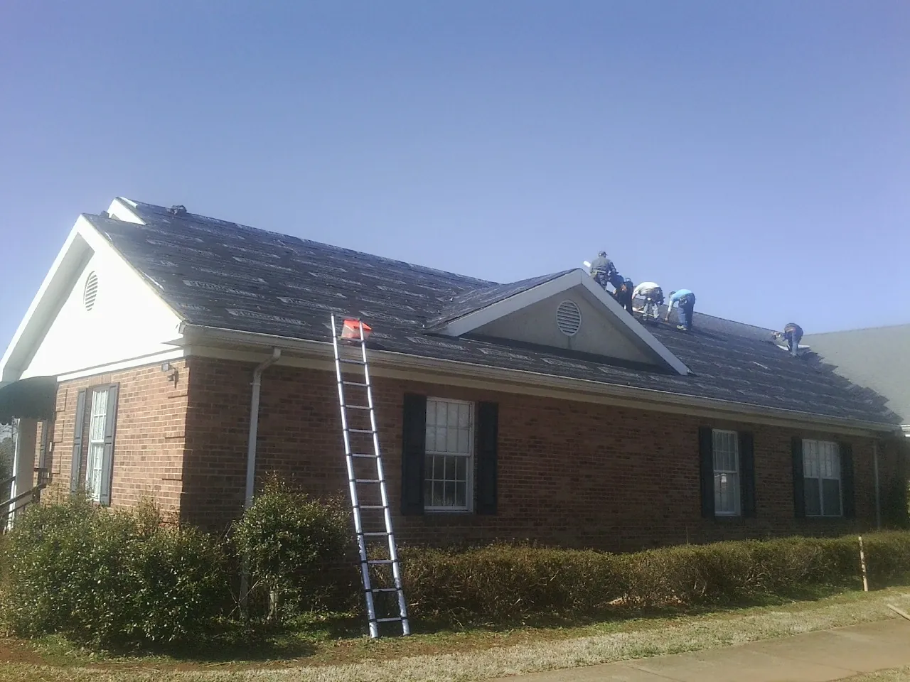 Crew tearing shingles off a brick ranch roof with a ladder set — Metal Roof Repair work by our crew in Mount Shasta