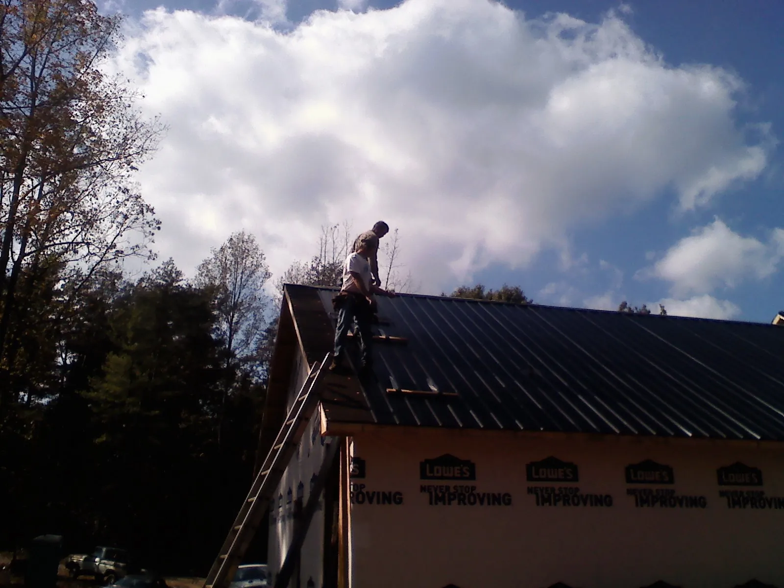 Roofer fastening dark metal panels high against a cloudy sky, from a Roof Inspection job in Mount Shasta